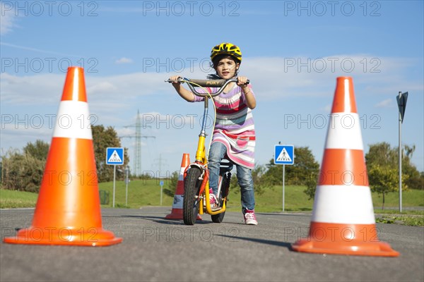 Girl practicing to ride slalom on a scooter at a traffic awareness course