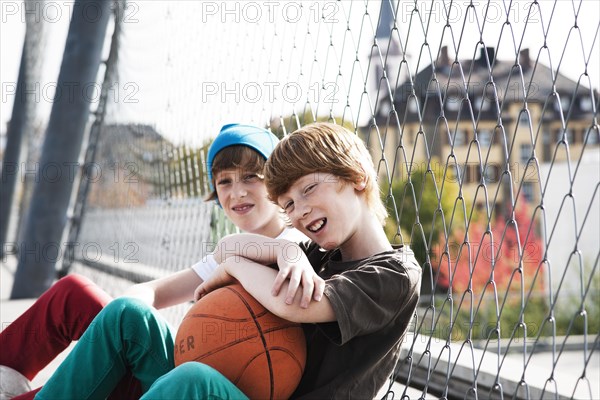 Two cool boys sitting with a basketball on a playground