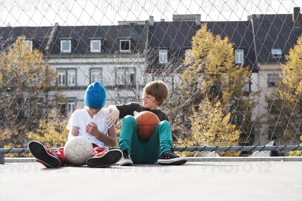 Two cool boys sitting with a basketball on a playground