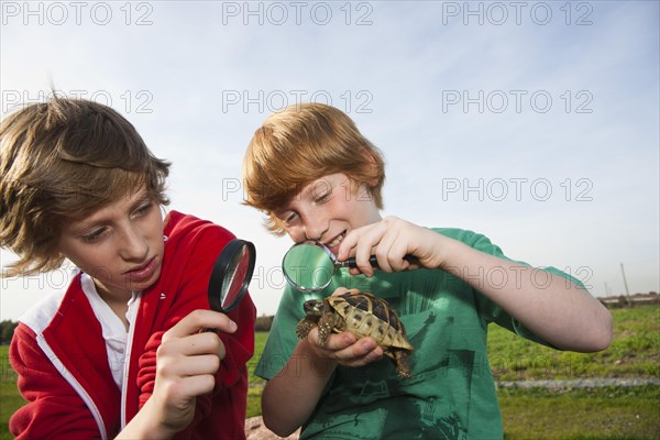 Two boys examining a turtle with a magnifying glass