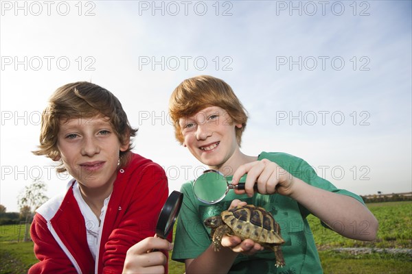 Two boys examining a turtle with a magnifying glass