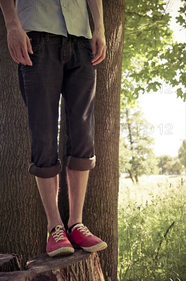 Lower section of young man standing on a tree stub