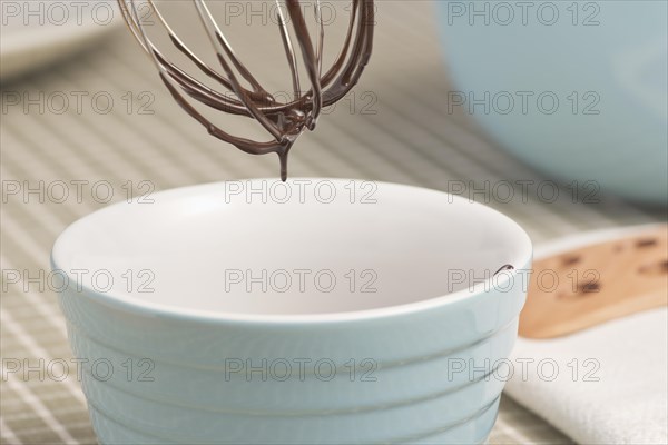 Dark chocolate dripping from wire whisk