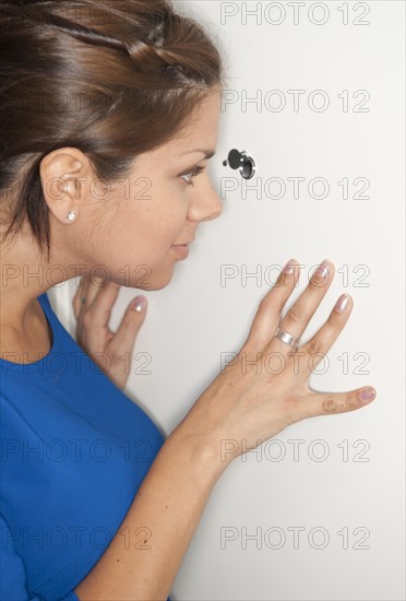 Woman peeking trough peephole in a door