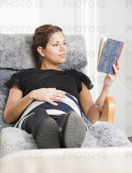 Pregnant woman lying in lounge chair and reading a diary