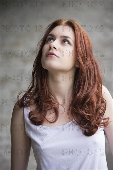 Pensive young woman with red hair looking up