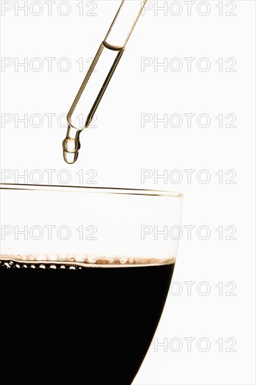 Pipette putting toxic substance in glass filled with red wine
