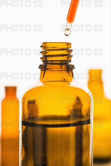 Dropper with red substance held over transparent brown bottle
