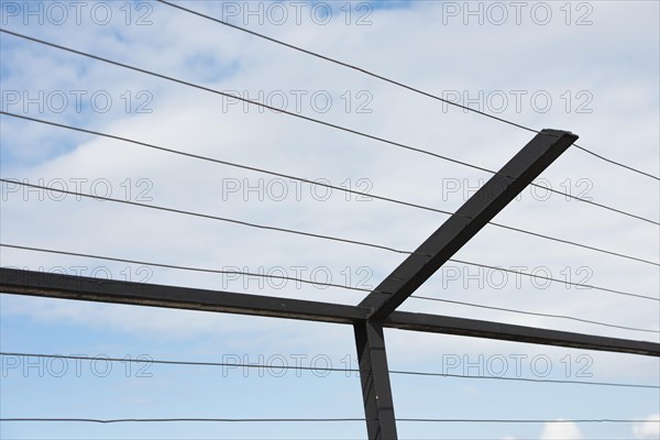 High fence with steel bars and wire against blue sky and clouds