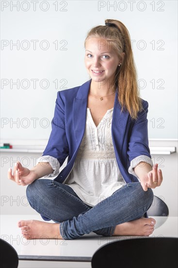 Businesswoman sitting barefoot in yoga position on her desk