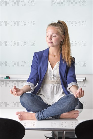 Businesswoman sitting barefoot in yoga position on her desk