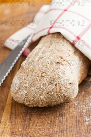 Fresh loaf of bread and kitchen knife on a wooden cutting board