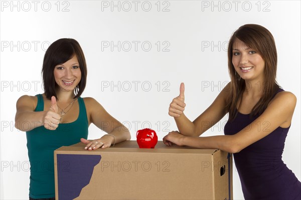 Two young woman with moving boxes and a piggy bank