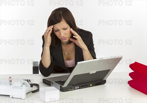 Young woman with a headache sitting at a desk with a laptop