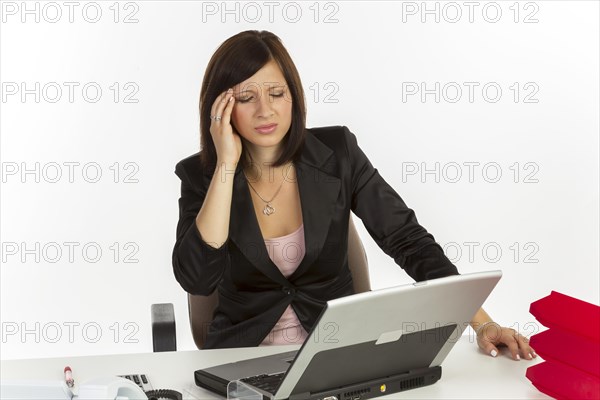 Young woman with a headache sitting at a desk with a laptop