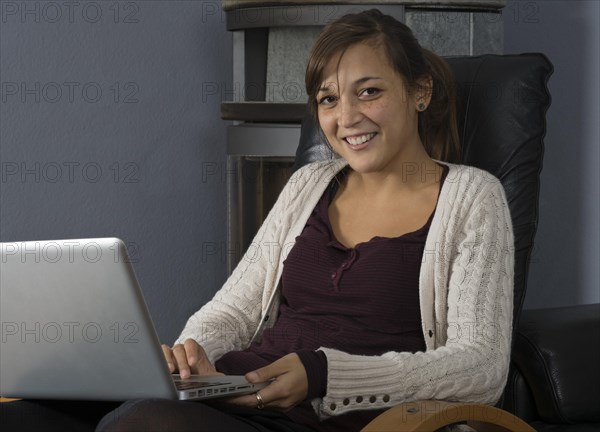 A young woman of Indonesian origin is sitting in front of a wood burner working on a laptop computer