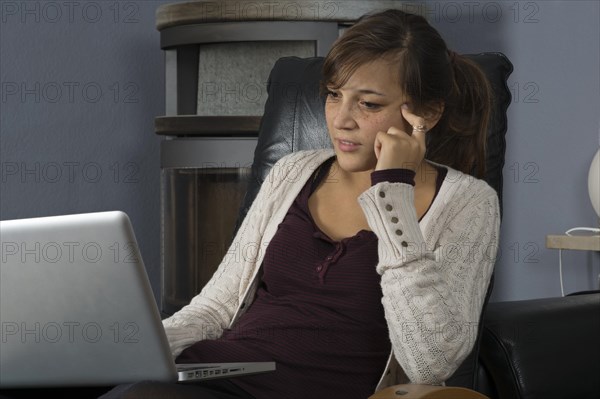 A young woman of Indonesian origin is sitting in front of a wood burner working on a laptop computer