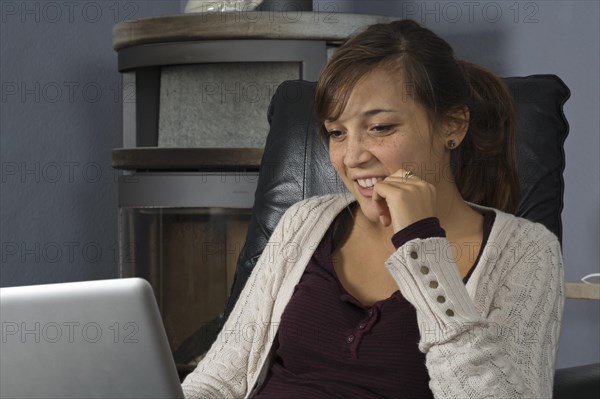 A young woman of Indonesian origin is sitting in front of a wood burner working on a laptop computer