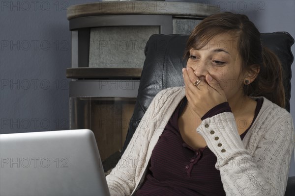 A young woman of Indonesian origin is sitting in front of a wood burner working on a laptop computer