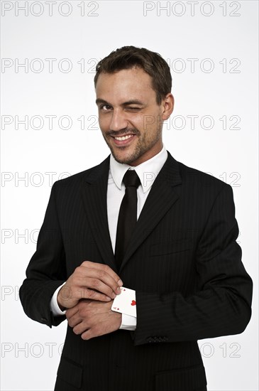 Man wearing a suit pulling an ace of hearts out of his sleeve