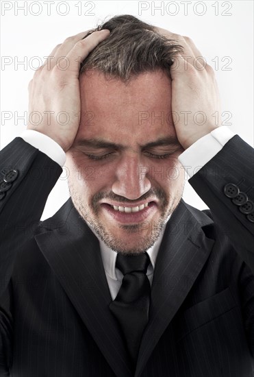 Desperate young man wearing a suit holding his hands to his face