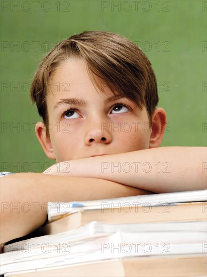 Schoolboy in front of a school blackboard with a stack of books