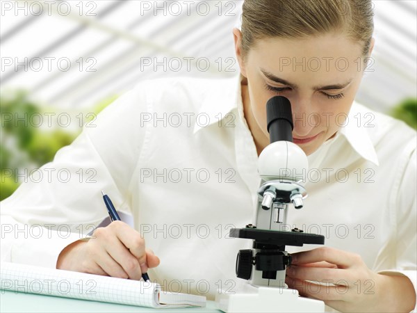 Scientist looking through a microscope in a greenhouse