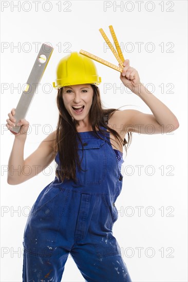 Woman wearing blue overalls and a hardhat holding a folding carpenter's ruler and a spirit level