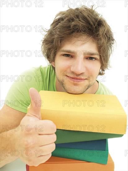 Young male student with a stack of books making a thumbs up gesture
