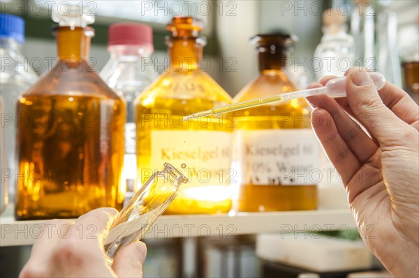 A laboratory worker using a pipette to fill a chemical liquid in a glass container