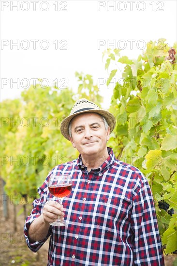 Winemaker or vintner standing with a glass of red wine in his vineyard