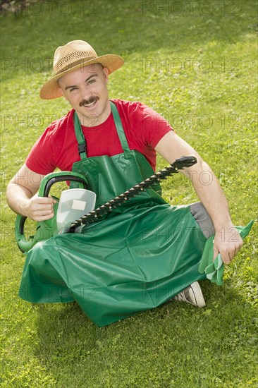 Gardener holding a hedge trimmer while sitting on the lawn