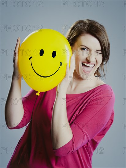 Smiling young woman holding a smiley face balloon