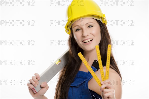 Woman wearing blue overalls and a hardhat holding a folding carpenter's ruler and a spirit level