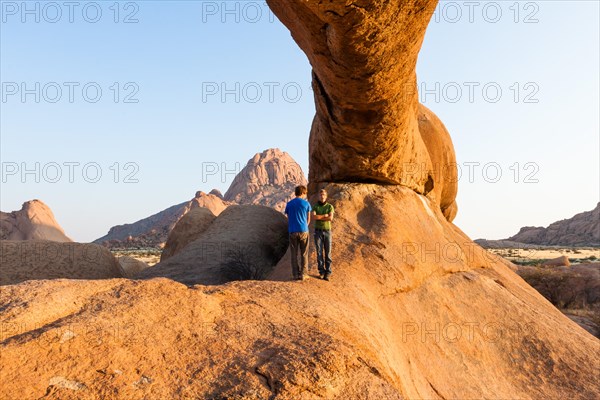 Two young men standing under a arch rock