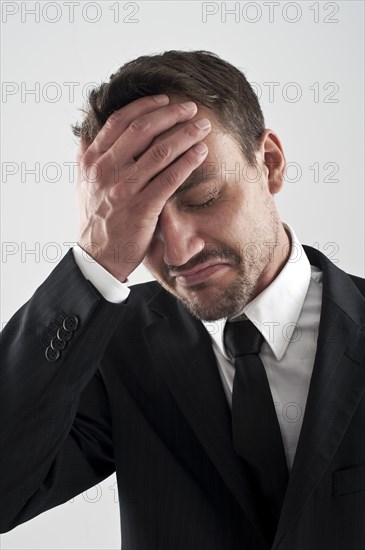 Young man wearing a suit holding his hand on his forehead