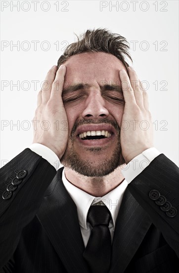 Desperate young man wearing a suit holding his hands to his face