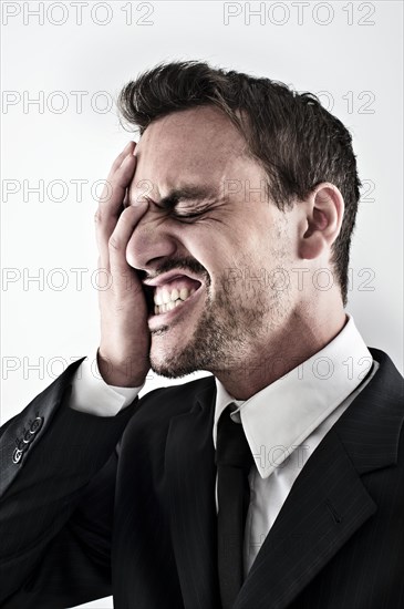 Desperate young man wearing a suit covering his face with his hand