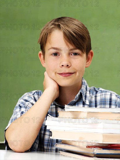 Schoolboy in front of a school blackboard with a stack of books