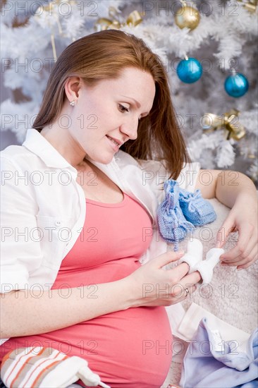 Pregnant woman with baby shoes sitting in front of a Christmas tree