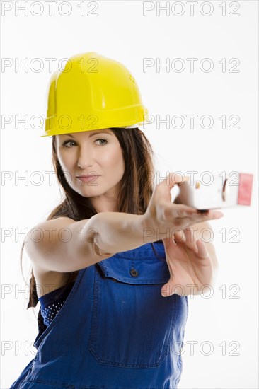 Woman wearing blue overalls and a hardhat holding a spirit level