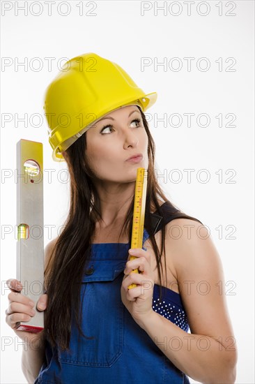 Woman wearing blue overalls and a hardhat holding a folding carpenter's ruler and a spirit level