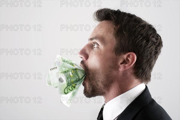 Young man wearing a suit with 100-euro notes stuffed into his mouth