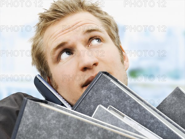 Businessman carrying ring binders while using a mobile phone