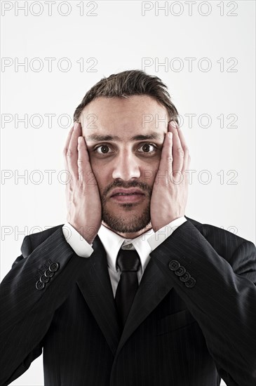 Desperate young man wearing a suit holding his hands to his face