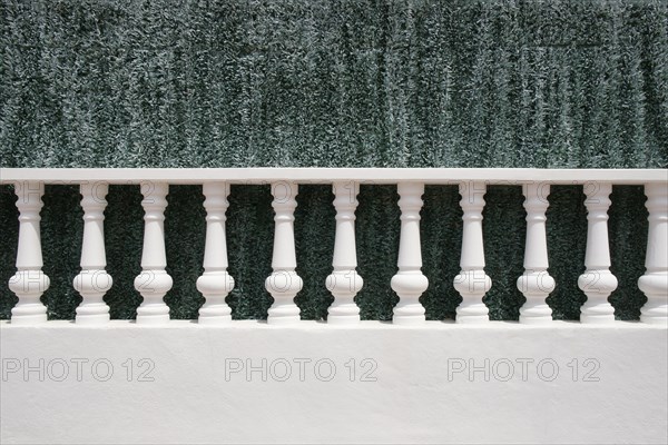 A white stone balustrade in front of an artificial green hedge