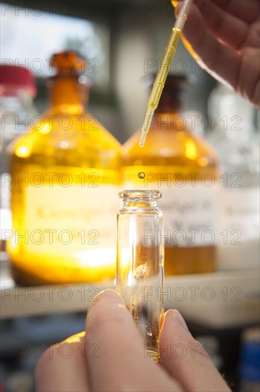 A laboratory worker using a pipette to fill a chemical liquid in a glass container