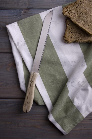 Bread knife and slices of bread with a kitchen towel on a wooden background