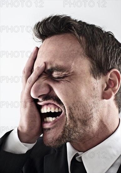 Desperate young man wearing a suit covering his face with his hand