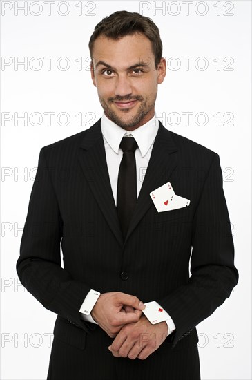 Man wearing a suit pulling an ace of diamonds out of his sleeve with other aces in his pocket